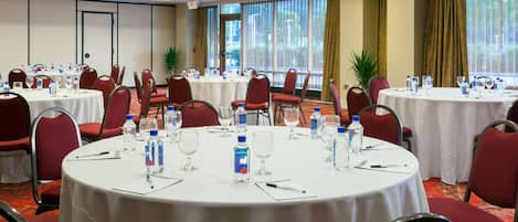 A conference room with round tables, red chairs, and white tablecloths.