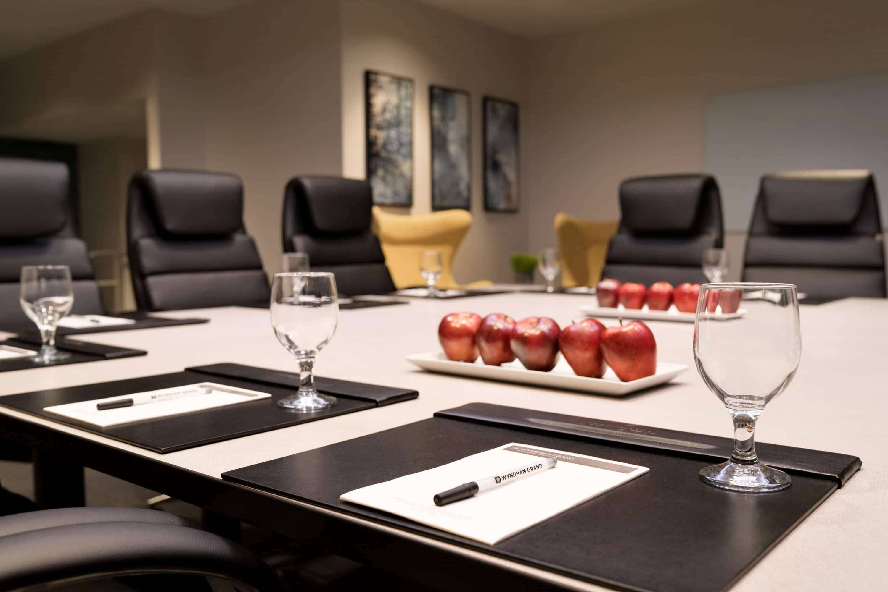 A conference room with a long table, black and yellow chairs, and a plate of red apples.