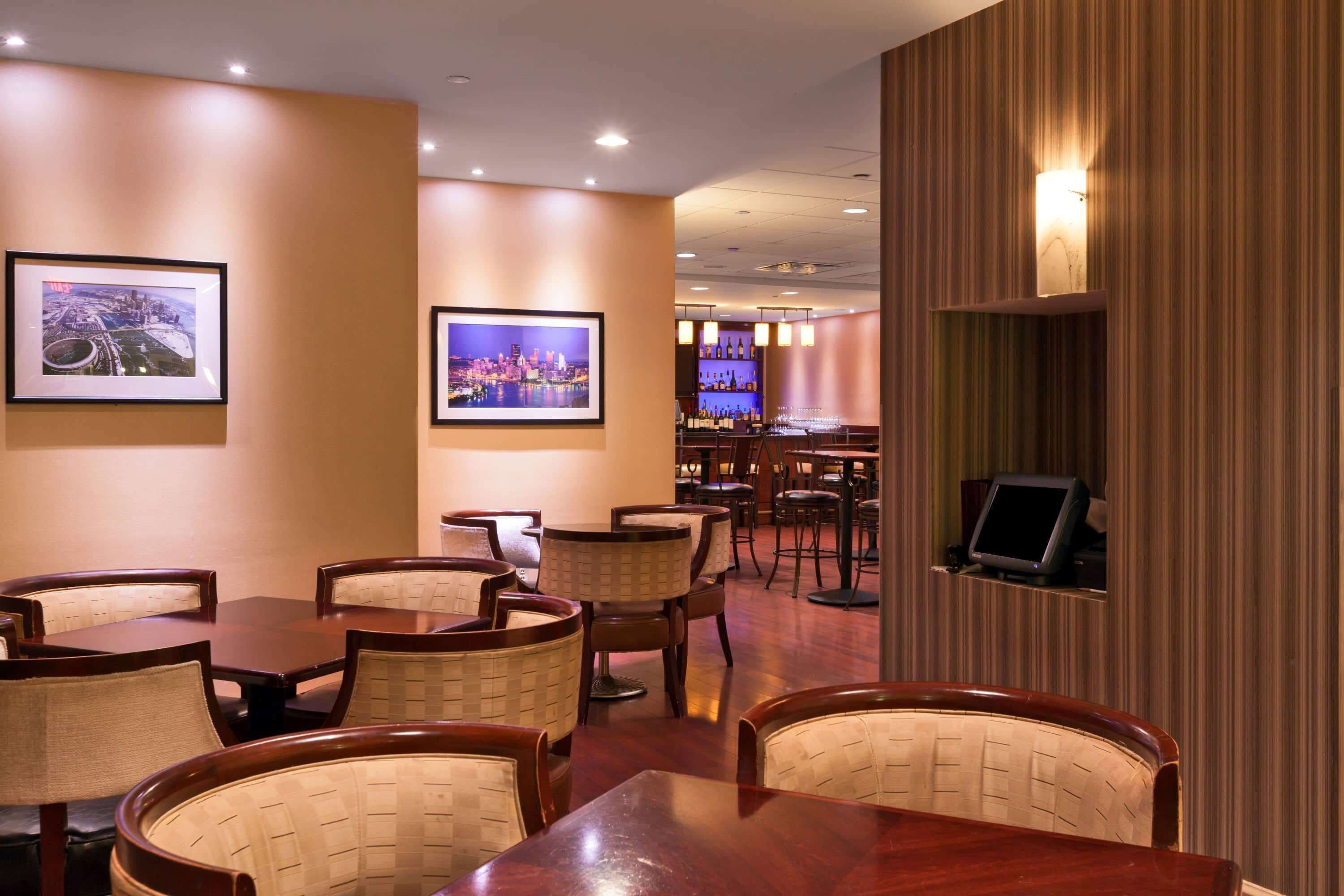 A restaurant with wooden tables and chairs, framed cityscape pictures on the walls, and a bar area in the background.