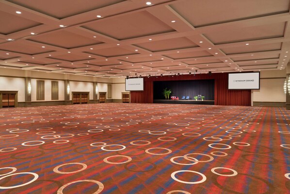 A large conference room with a patterned carpet, a stage with a screen, and a banner reading "Wyndham Grand."