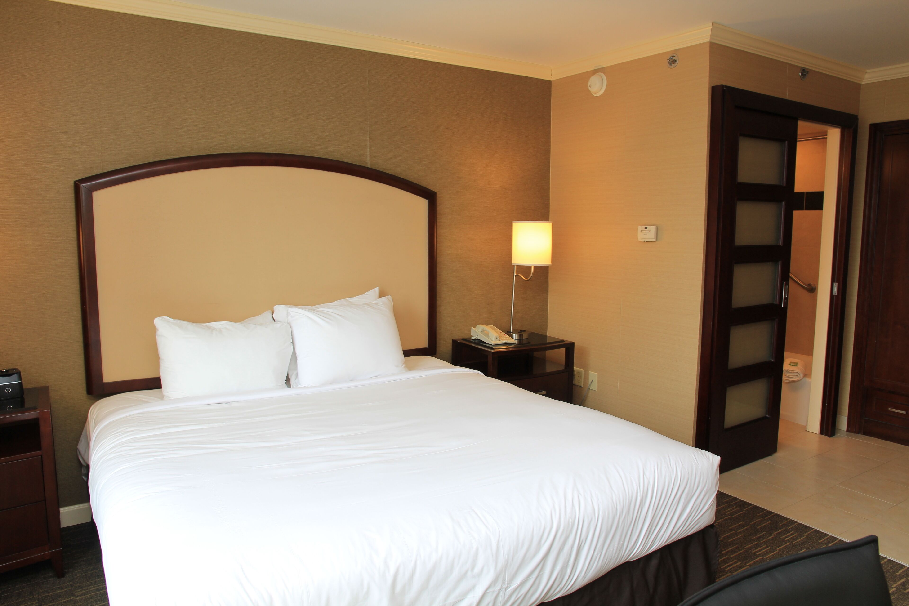Une chambre d’hôtel avec un grand lit, une table de chevet avec une lampe et une porte donnant sur une autre pièce.