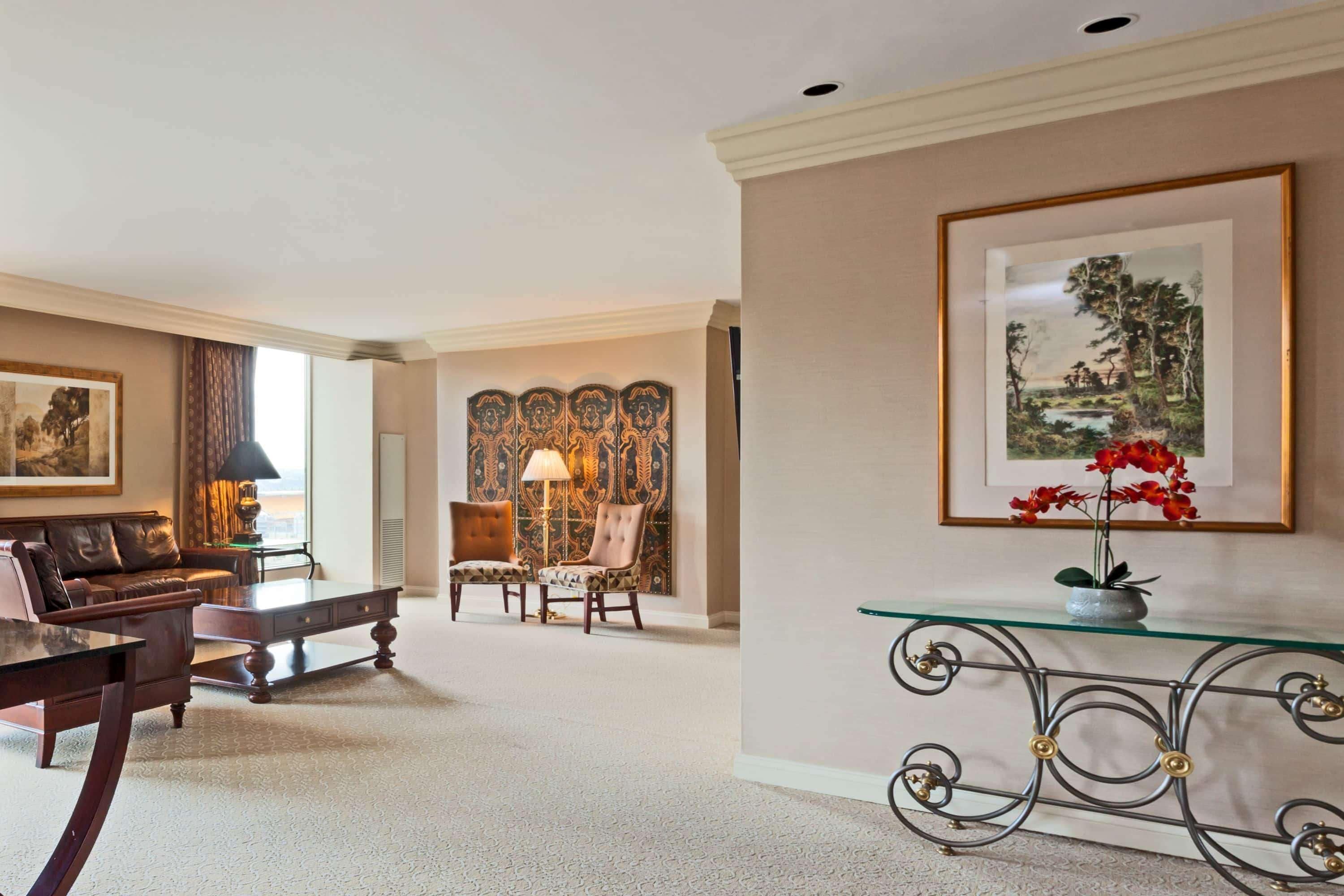 A spacious living room with a leather sofa, a glass coffee table, and a decorative wall panel.