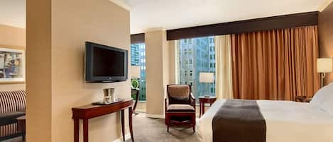 A hotel room with a bed, a television, a desk, a chair, and a window with curtains.