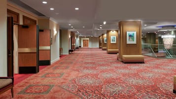 Un pasillo de hotel con alfombra roja de diseño, paredes de madera y una escalera con barandas de vidrio.