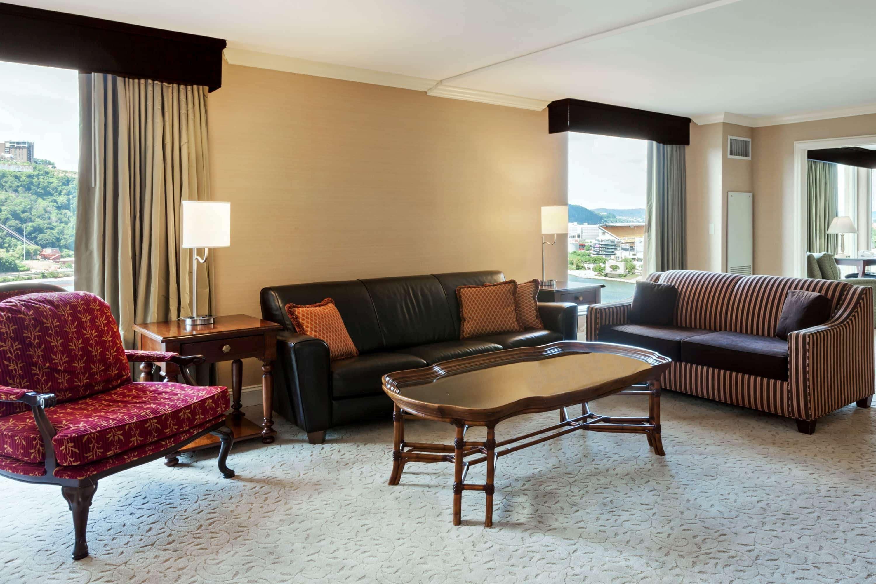 A hotel room with a red armchair, a black leather sofa, a striped sofa, and a wooden coffee table.