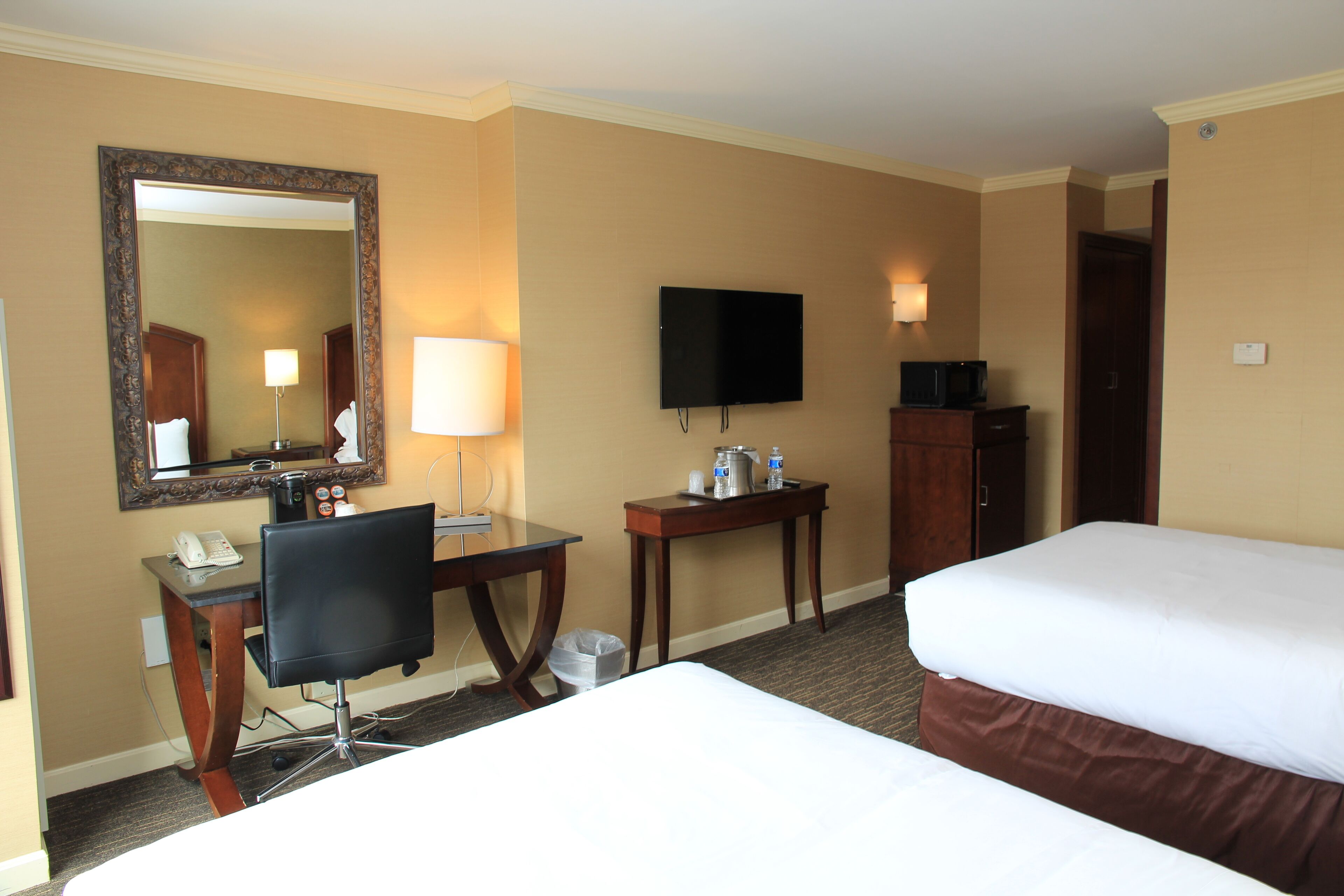 Habitación de hotel con escritorio, silla, dos camas, televisor y espejo.
