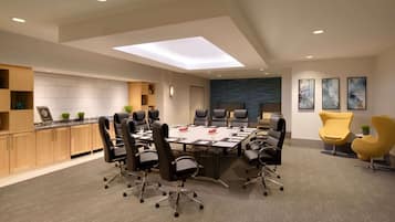 A modern conference room with a large table, black office chairs, a skylight, wooden cabinets, and artwork on the walls.