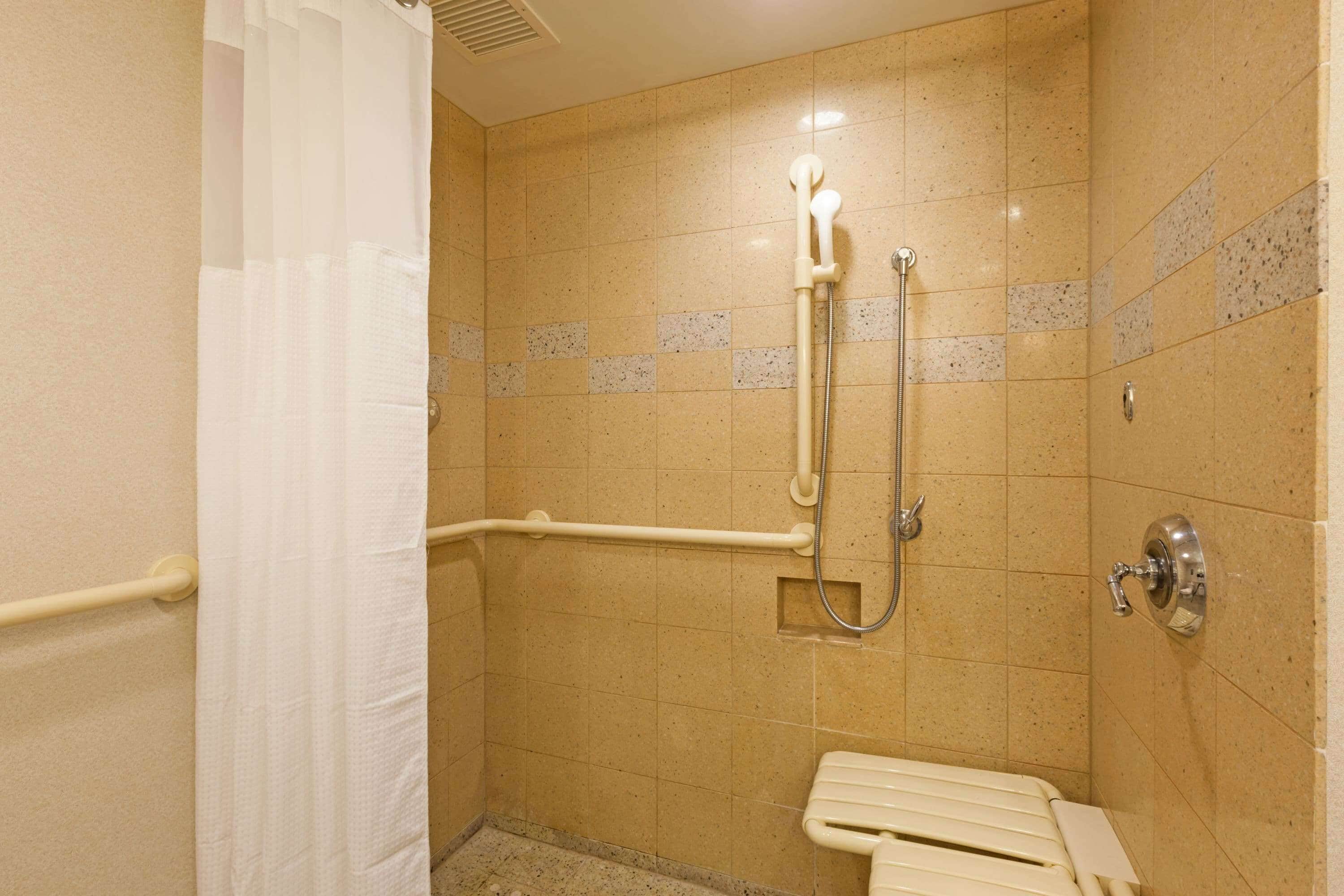 Un baño pequeño y accesible con ducha, barras de apoyo y un inodoro.