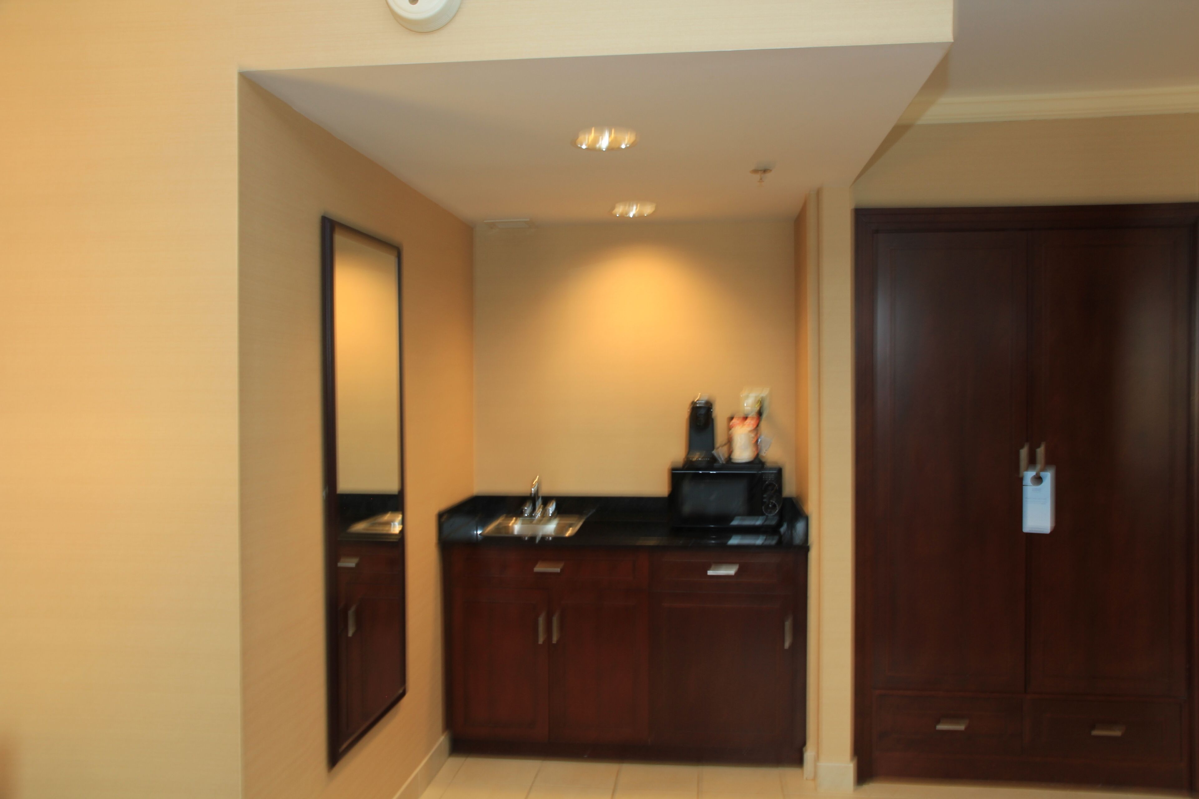 Una habitación de hotel con kitchenette, un espejo grande y un armario.