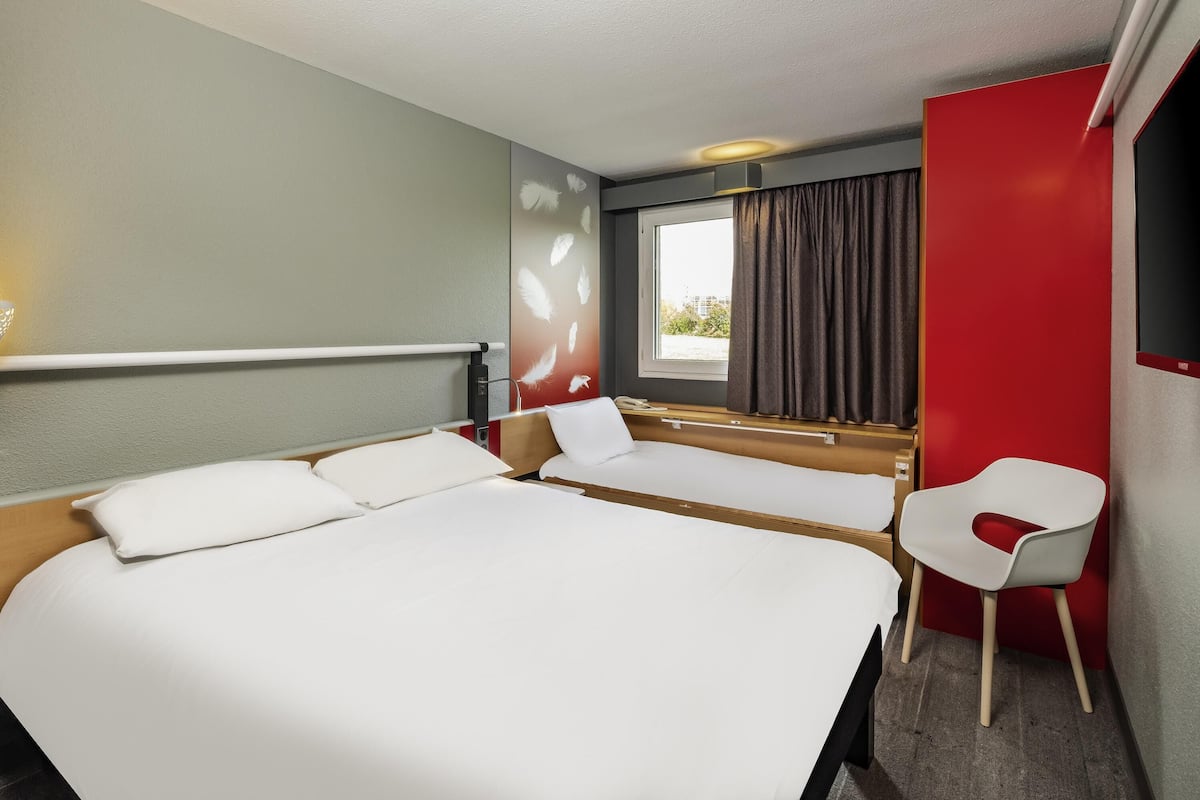 A hotel room with a large bed, a bedside table, a chair, a window with curtains, and a wall-mounted TV.