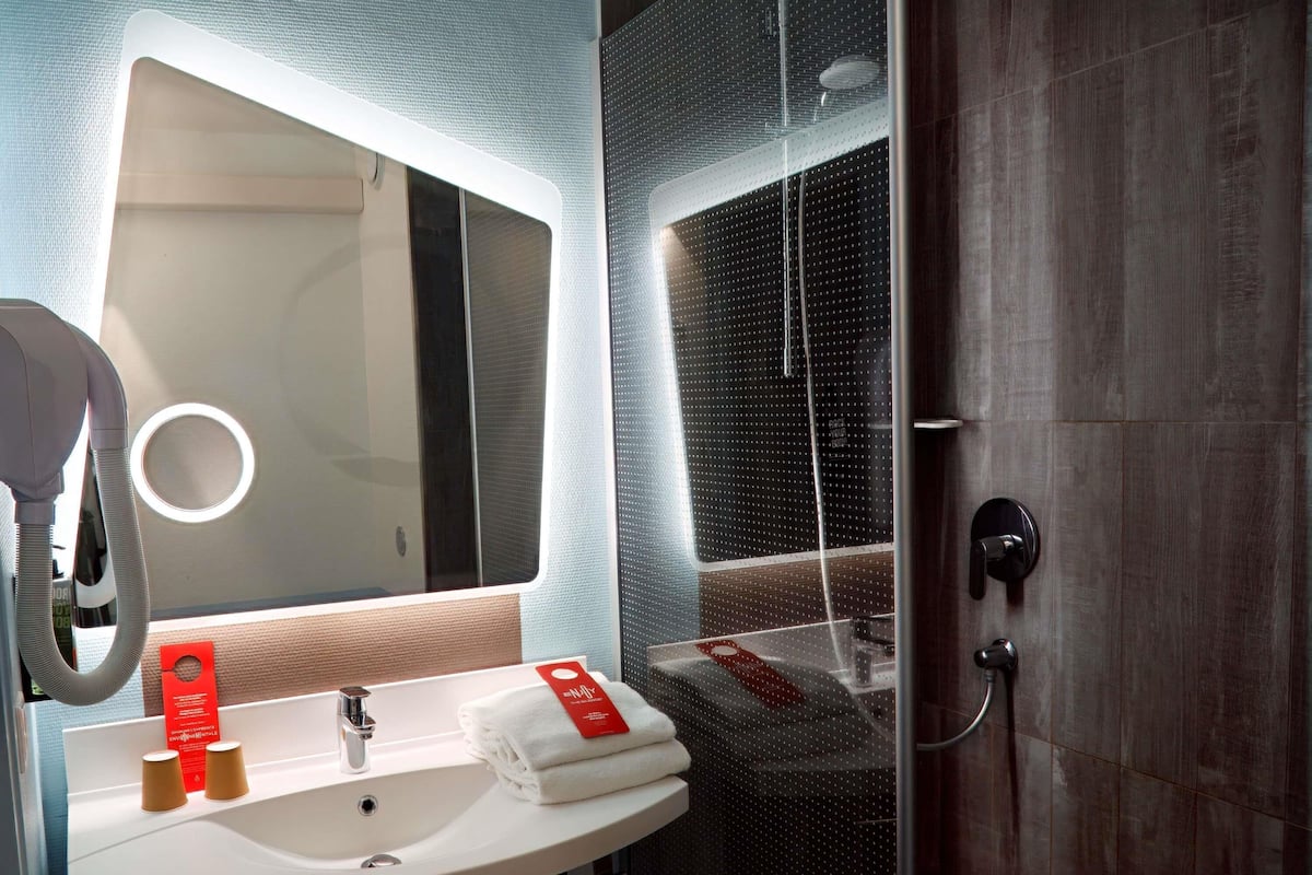 A modern bathroom with a white sink, a mirror, and a shower area.