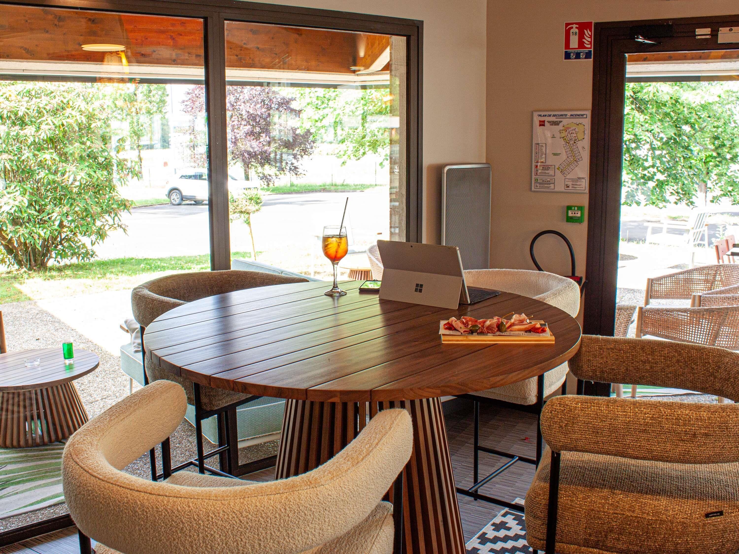A round wooden table with a laptop, a glass with a straw, and a plate of food. There are wicker chairs around the table.
