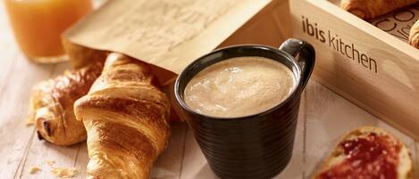 Croissants, a cup of coffee, and a wooden box labeled "ibis kitchen" on a wooden surface.