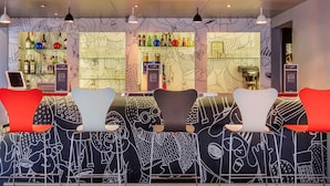 A bar area with modern chairs, a bar counter, and a wall with abstract art. - Ibis Amboise (Amboise)