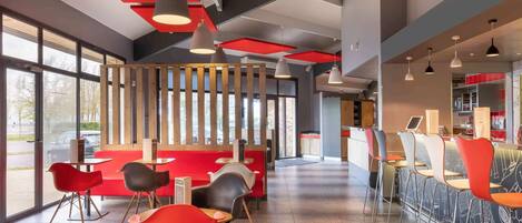 A modern restaurant interior with red and black chairs, a bar area, and large windows.
