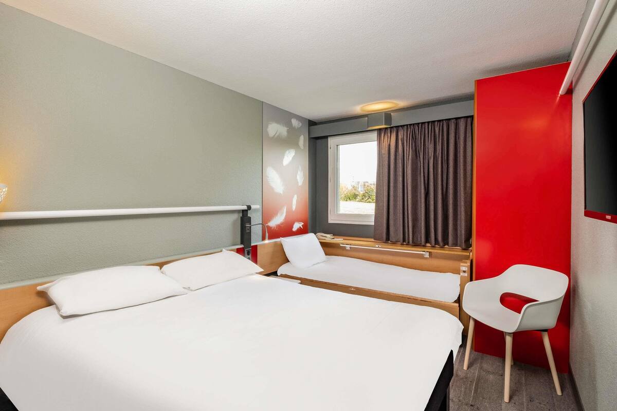 A hotel room with a large bed, a desk, a chair, and a window with curtains.