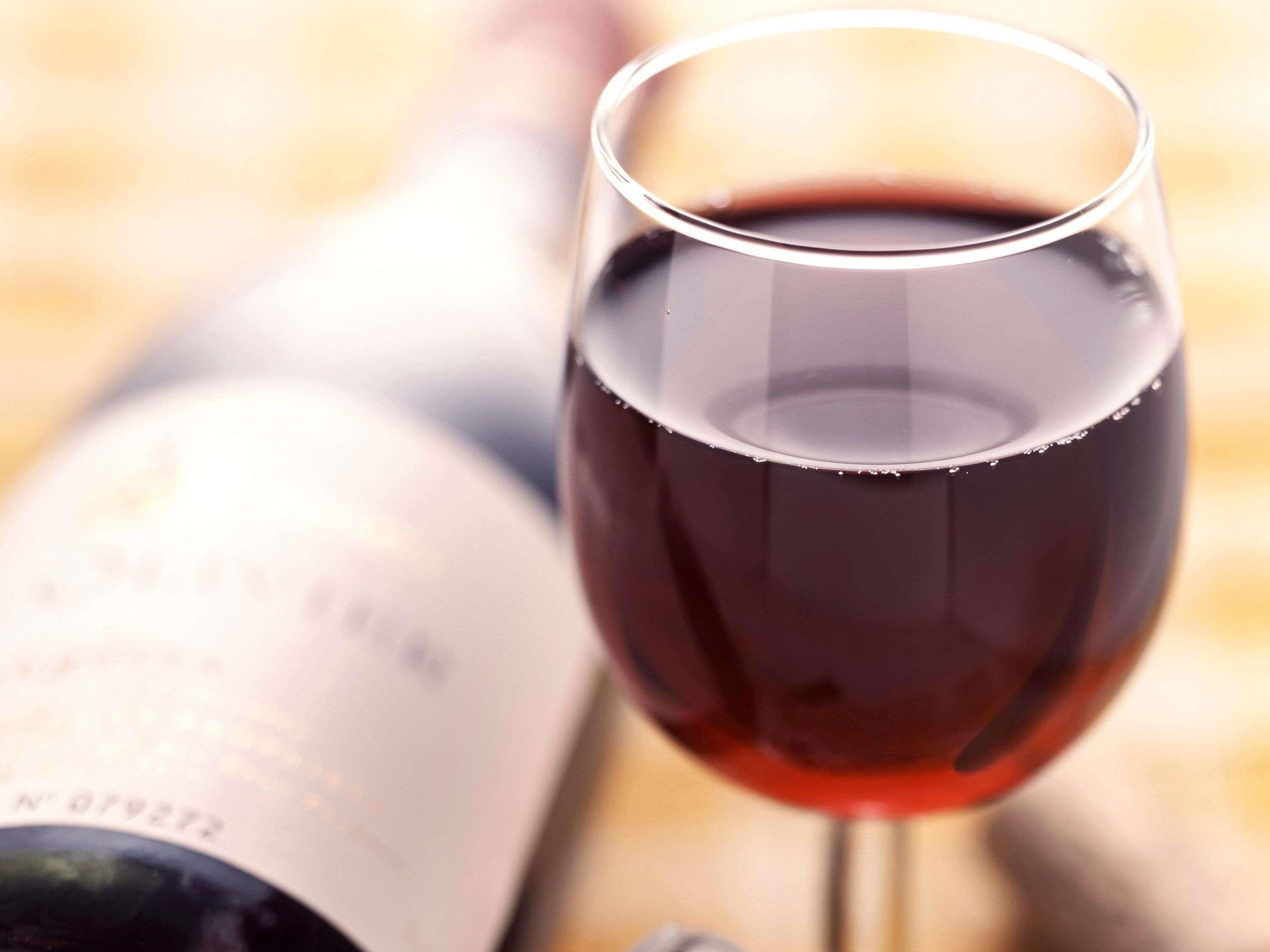 A wine glass filled with red wine and a bottle in the background.