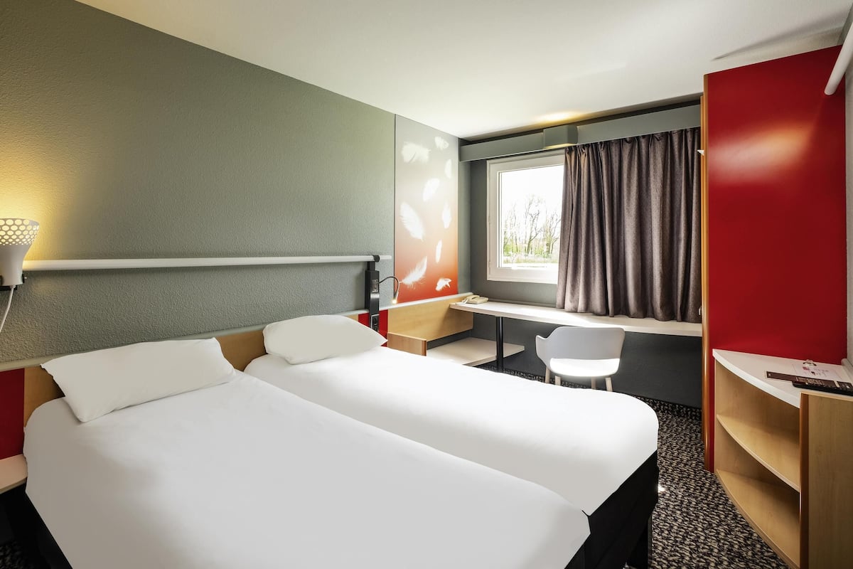 A hotel room with a bed, desk, chair, and a window with curtains.