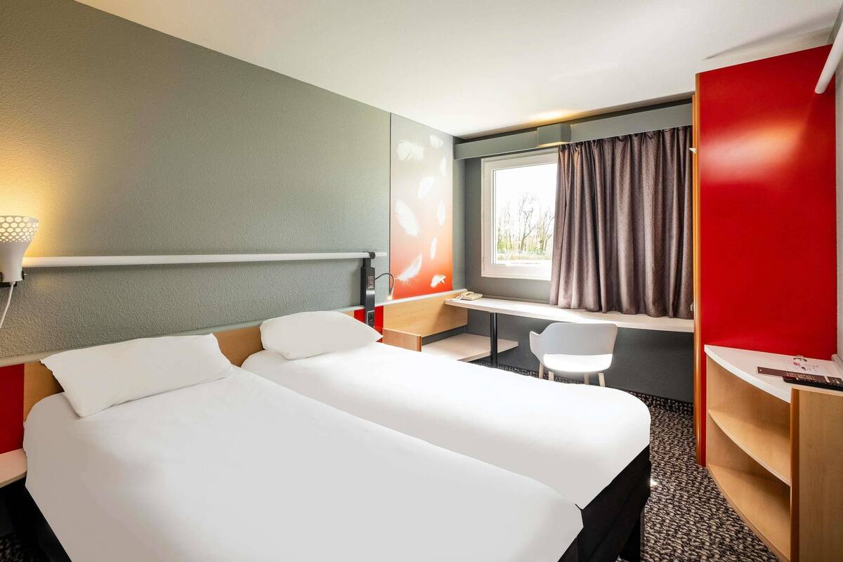 A hotel room with a bed, desk, chair, and a window with curtains.