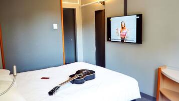 Una habitación de hotel con una cama, una guitarra, un televisor y una mesita de noche.