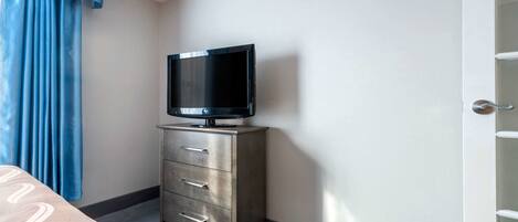 A hotel room with a flat-screen TV on a metallic cabinet, a bed with a patterned bedspread, and a blue curtain.