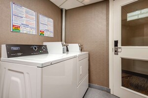 A laundry area with a Maytag washer and dryer, two informational posters on the wall, and a door with a window.
