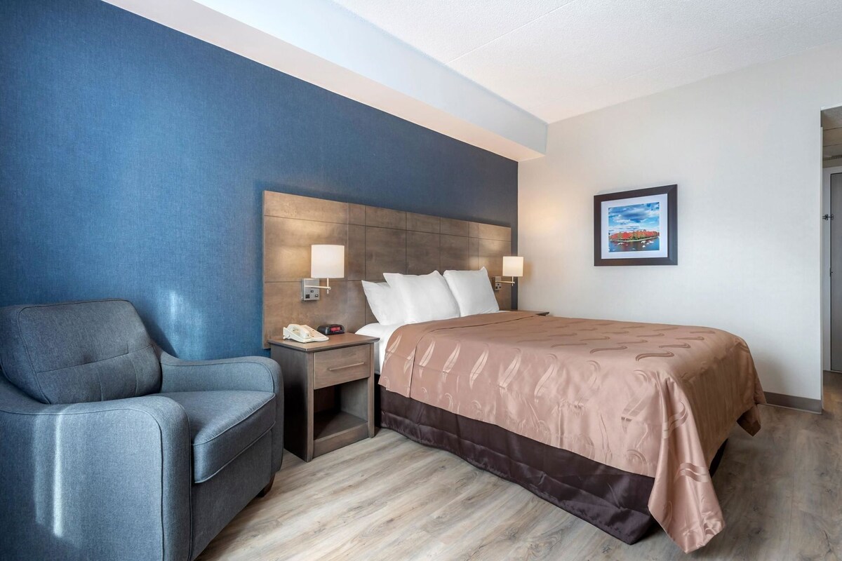 A hotel room with a bed, a desk with a telephone, a chair, and a wall-mounted lamp.