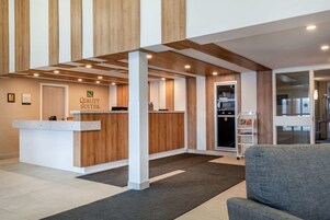A reception area with a wooden reception desk, a grey sofa, and a wall-mounted sign that reads "Quality Suites."