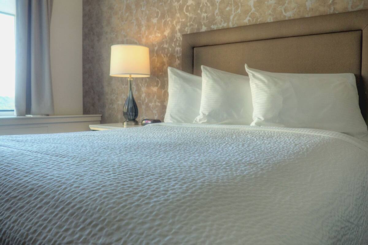 A neatly made bed with a textured white duvet, a bedside lamp, and a headboard.