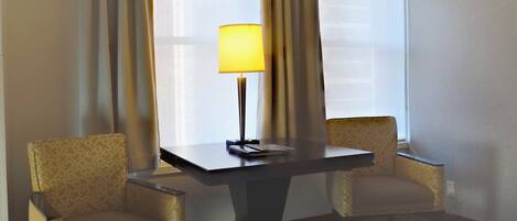 A hotel room with a bed, a table with a lamp, and two patterned armchairs.