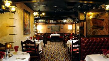 A restaurant interior with multiple tables, red upholstered booths, patterned carpet, and wall-mounted lighting fixtures.