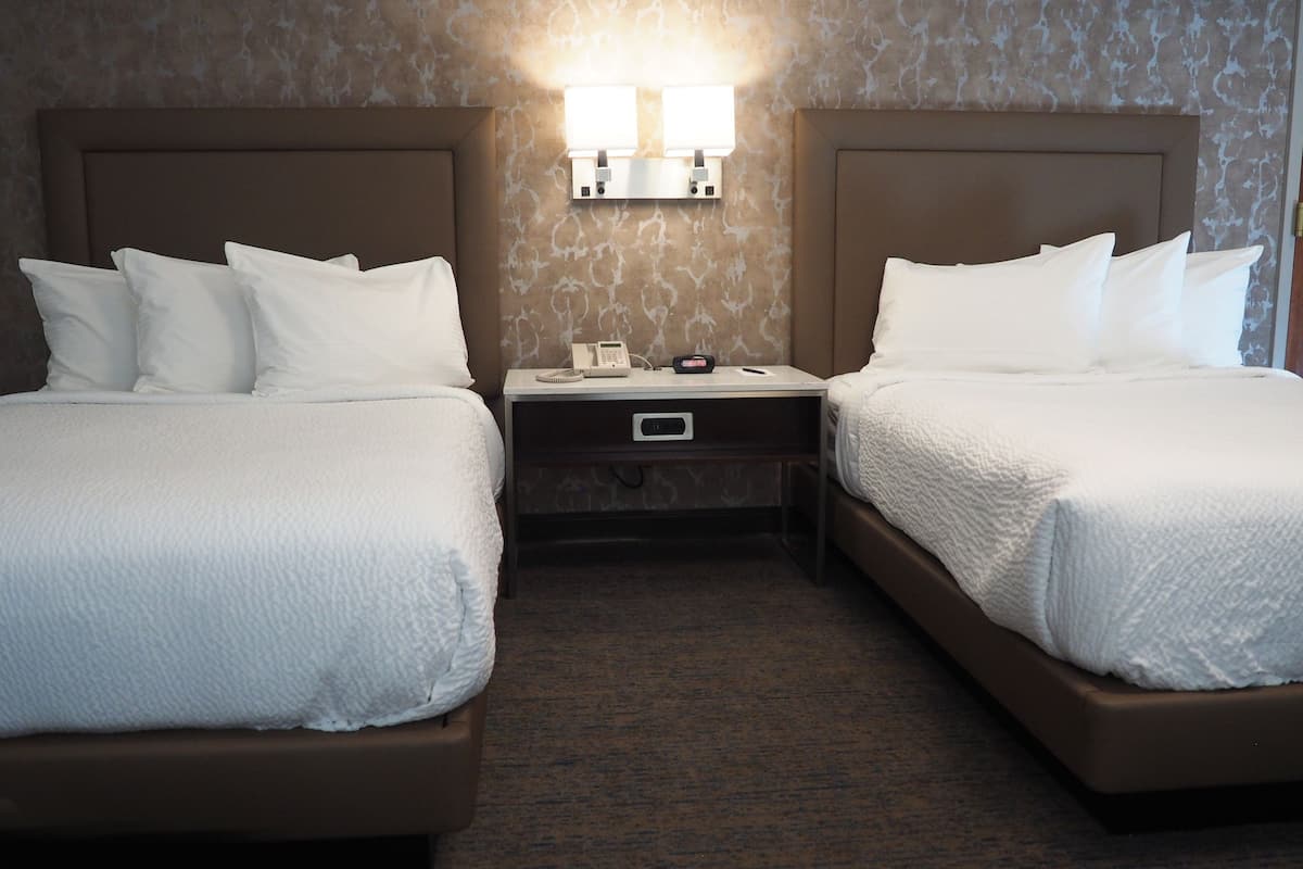 A hotel room with two beds, a nightstand with a lamp, and a telephone.