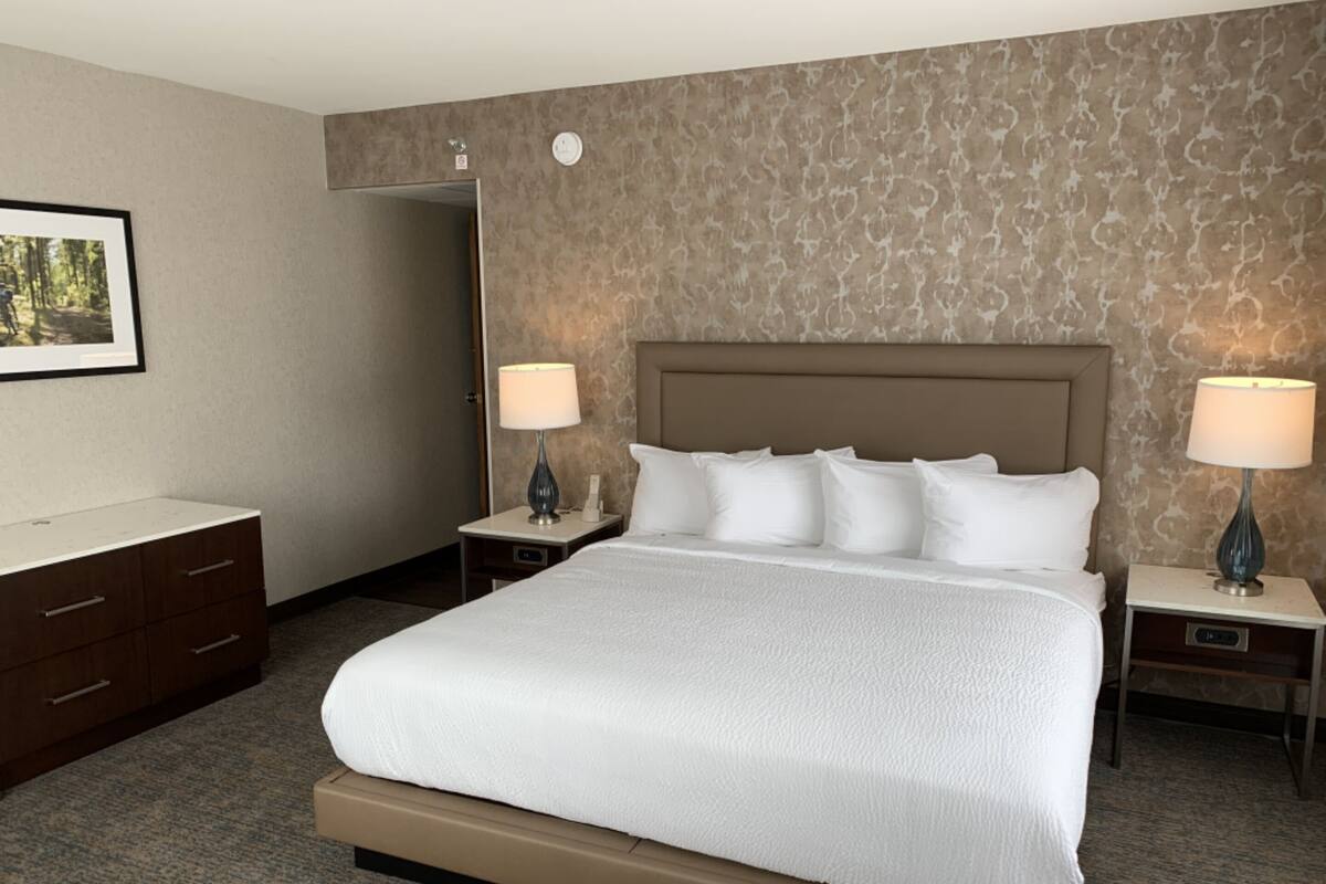 A hotel room with a large bed, two bedside tables with lamps, a dresser, and a framed picture on the wall.