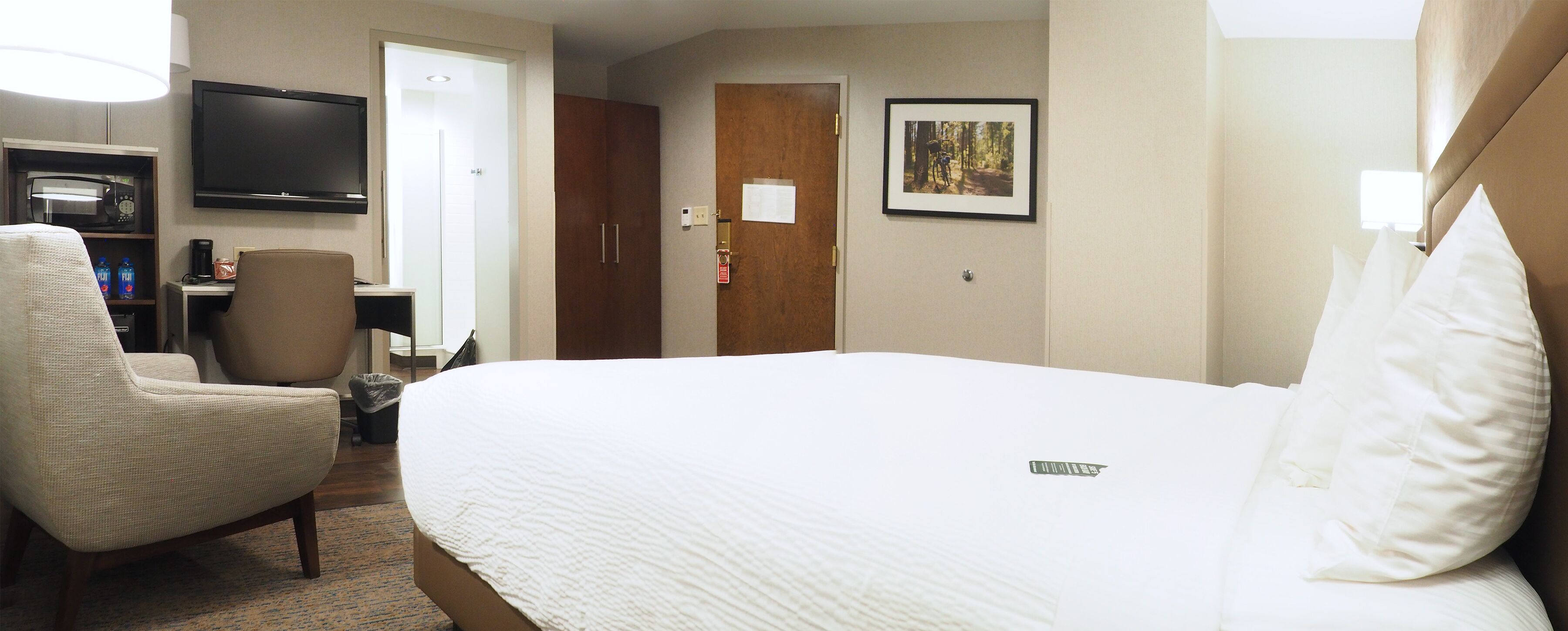 Habitación de hotel con una cama, una silla, un escritorio con computadora, televisor y puerta.