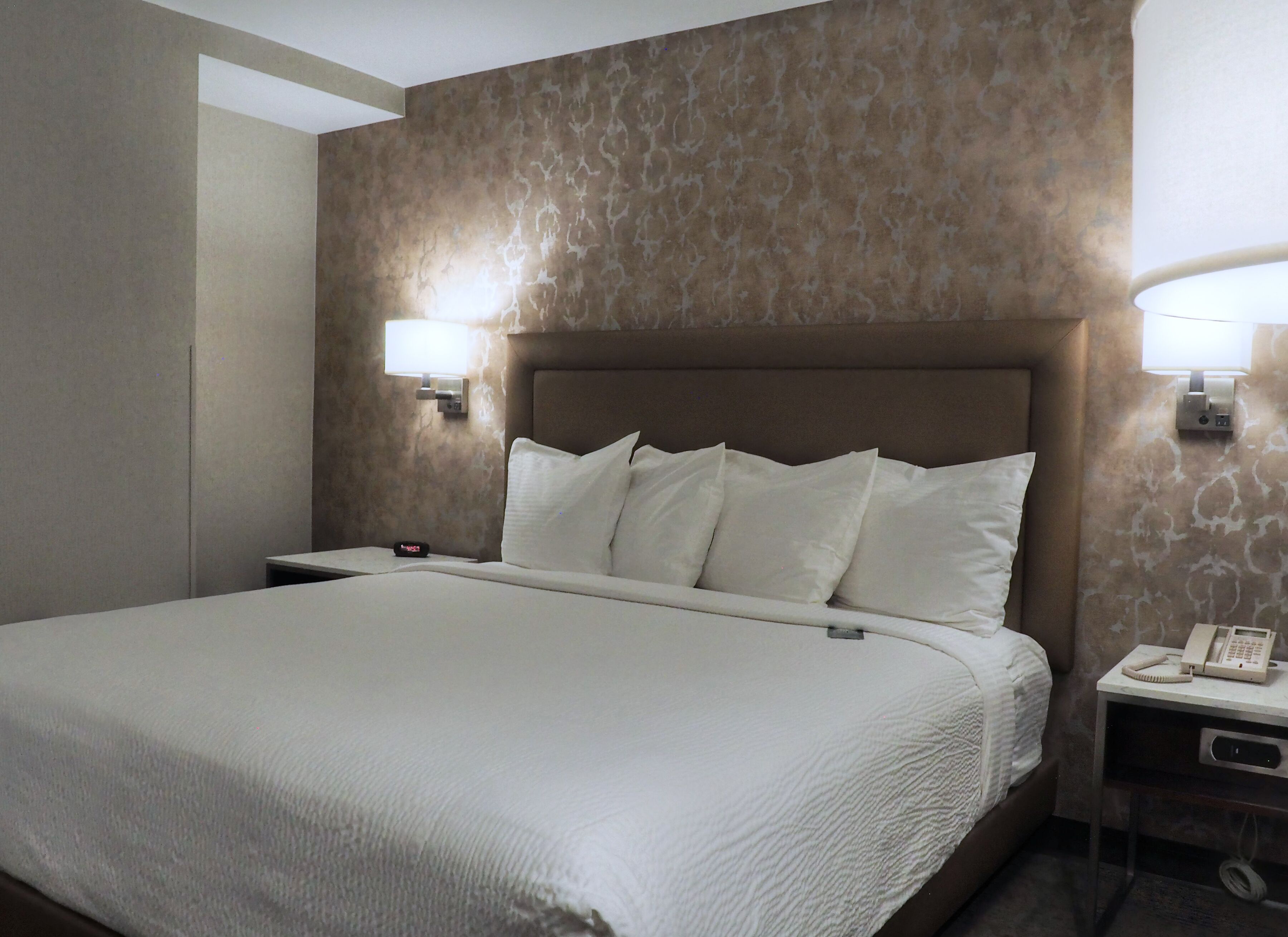 Une chambre d’hôtel avec un grand lit, deux lampes de chevet, une table de chevet avec un téléphone et un mur à motifs.