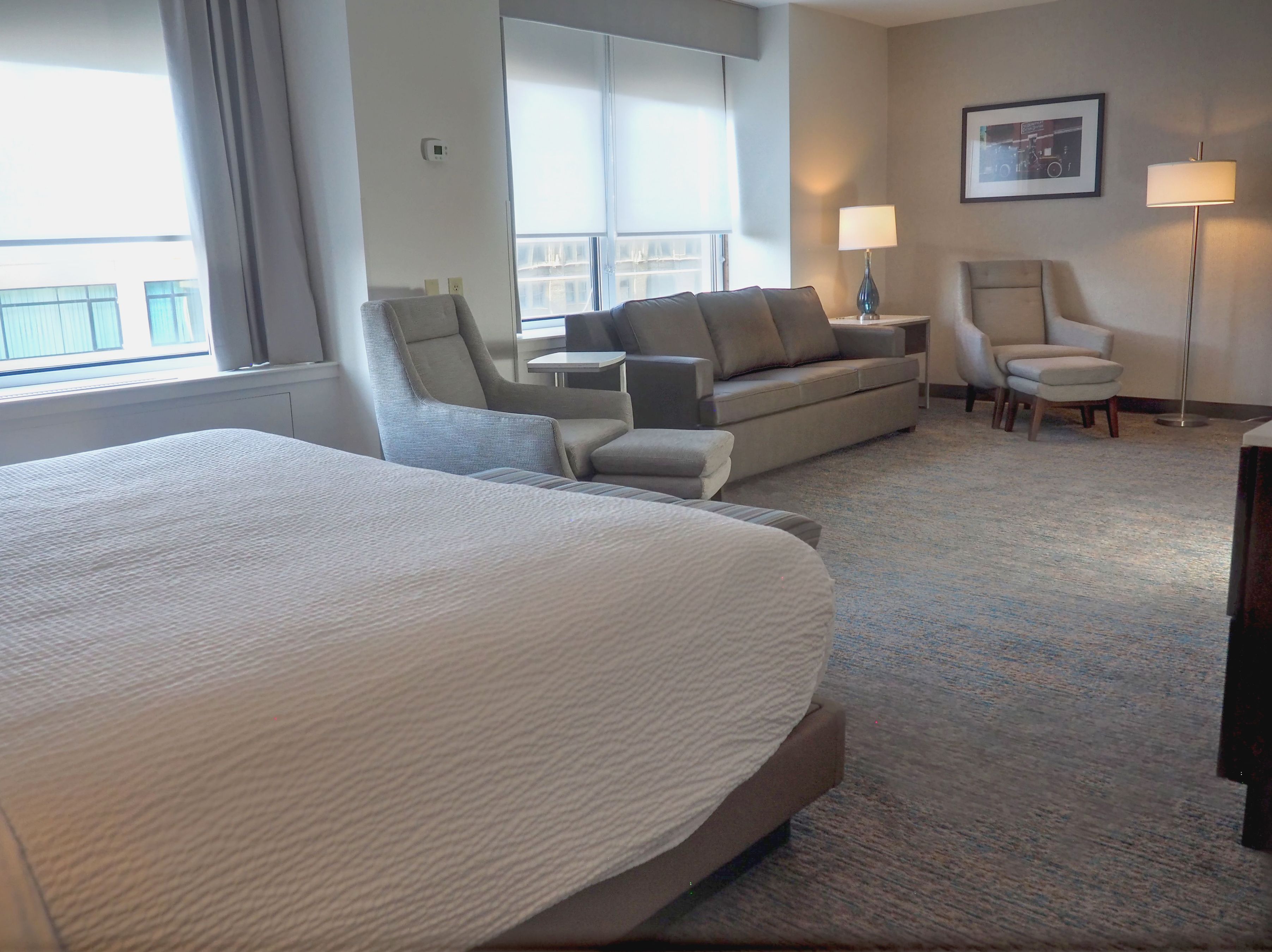 A hotel room with a large bed, a sofa, two armchairs, a small table, and a lamp.