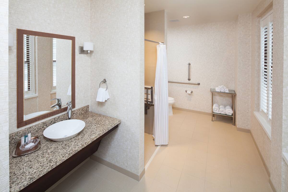 A bathroom with a granite countertop, a white sink, a large mirror, a shower with a glass door, and a towel rack with towels.