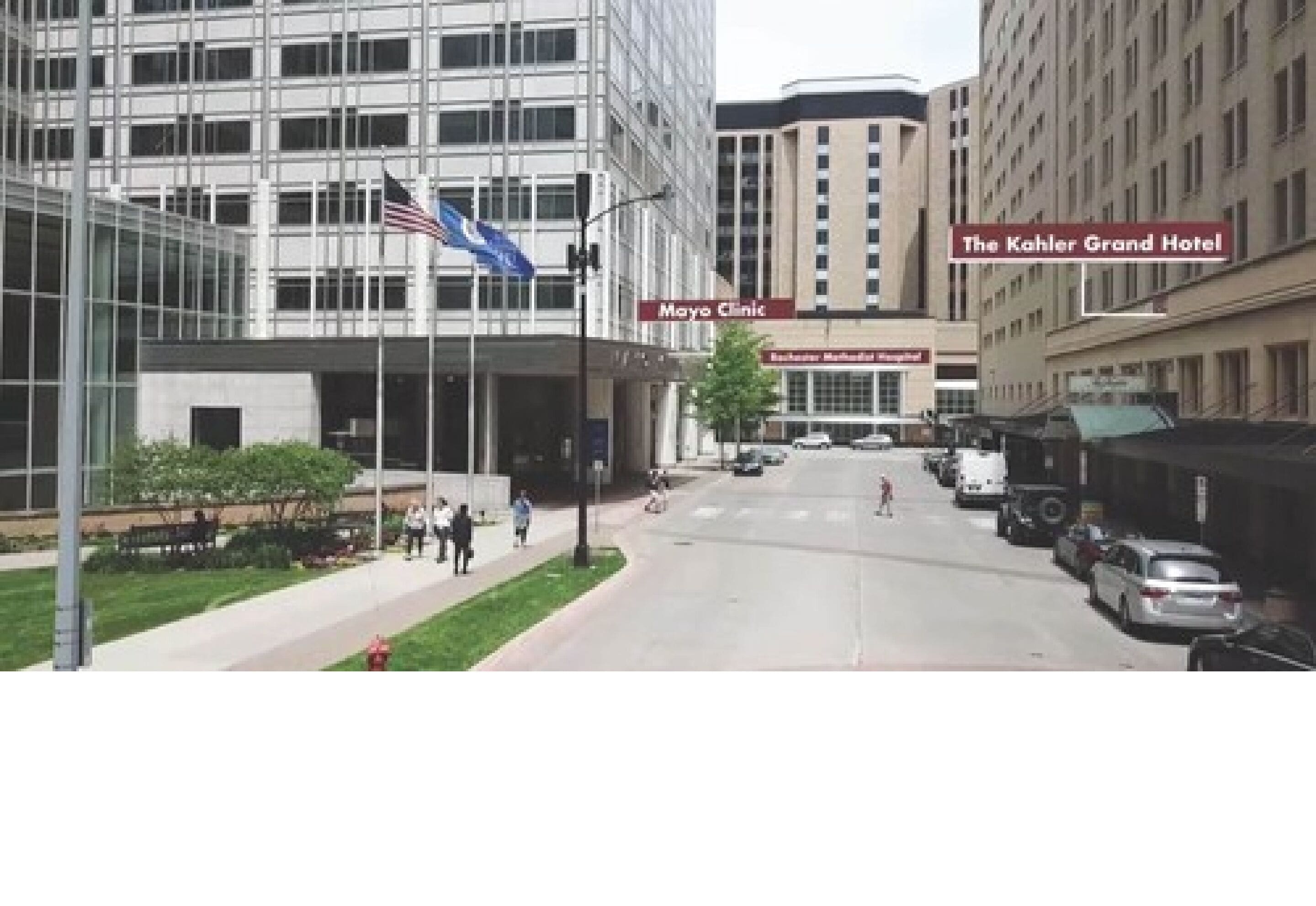 A modern building with a glass facade, a flag, and signs for 'Mayo Clinic' and 'The Kahler Grand Hotel'.