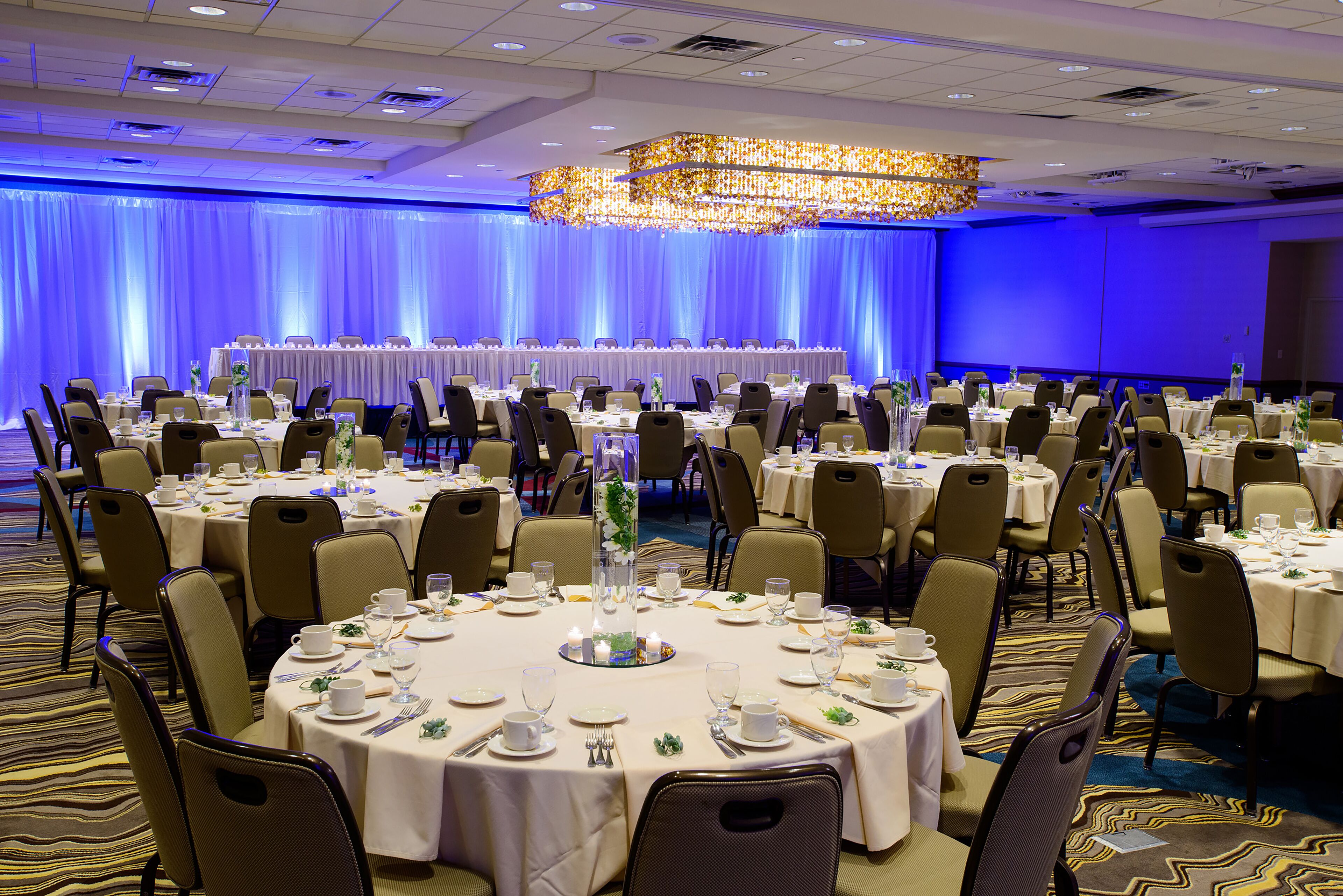 Une salle de banquet avec des tables rondes disposées en rangées, prêtes pour le repas.