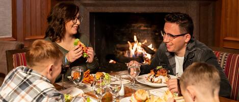 Una familia comiendo en una mesa con una chimenea al fondo.