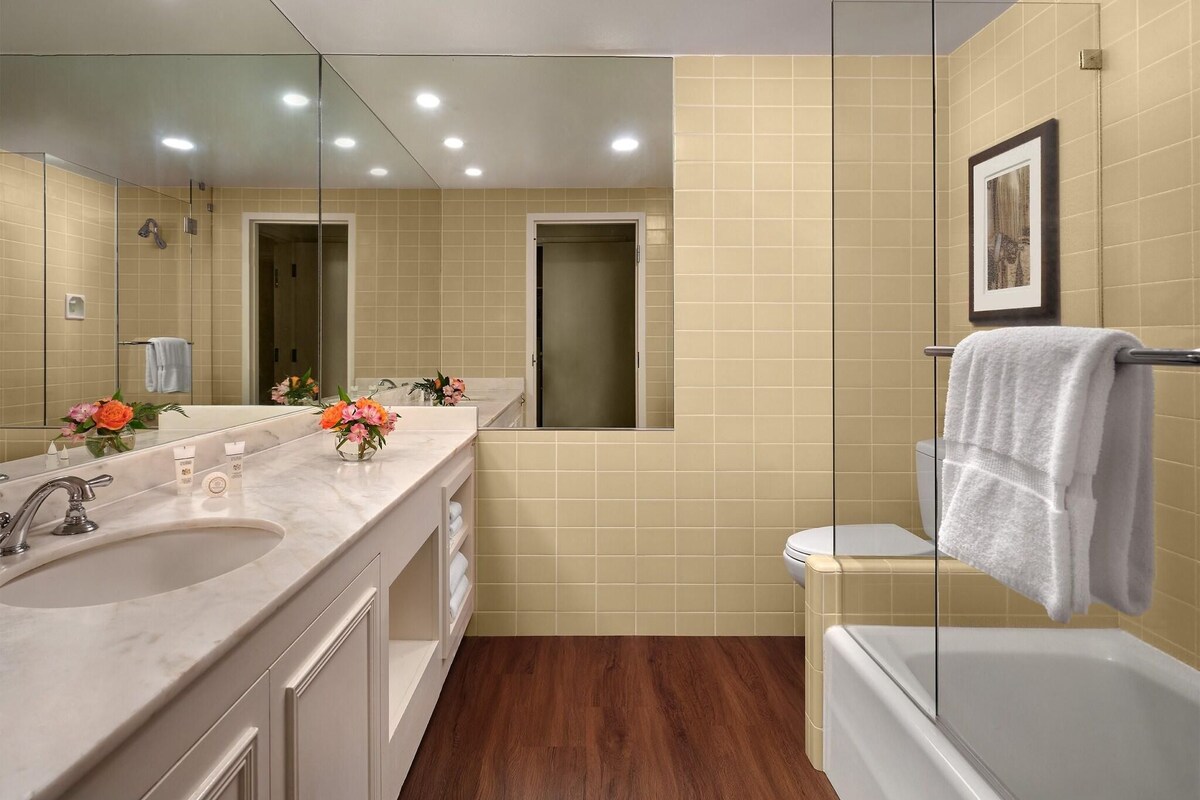 A modern bathroom with a large mirror, two sinks, a shower, and a toilet.