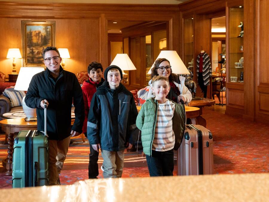 A group of people with luggage in a hotel lobby with wooden decor, lamps, and a painting on the wall.