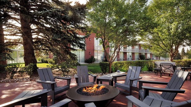 An outdoor seating area with Adirondack chairs and a central fire pit. - Little America Cheyenne (Cheyenne)
