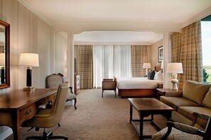 A hotel room with a bed, two bedside tables, a desk, a chair, a sofa, and a large window with curtains.