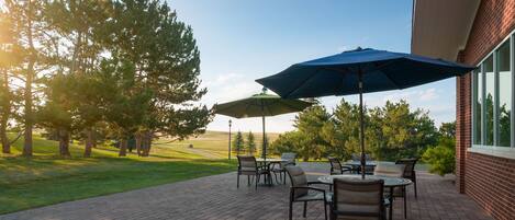 An outdoor patio with brick flooring, outdoor furniture, and umbrellas.