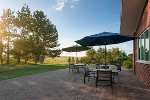 An outdoor patio with brick flooring, outdoor furniture, and umbrellas.