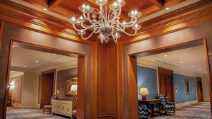 A grand hallway with a chandelier, wooden paneling, and a patterned carpet. - Little America Cheyenne (Cheyenne)