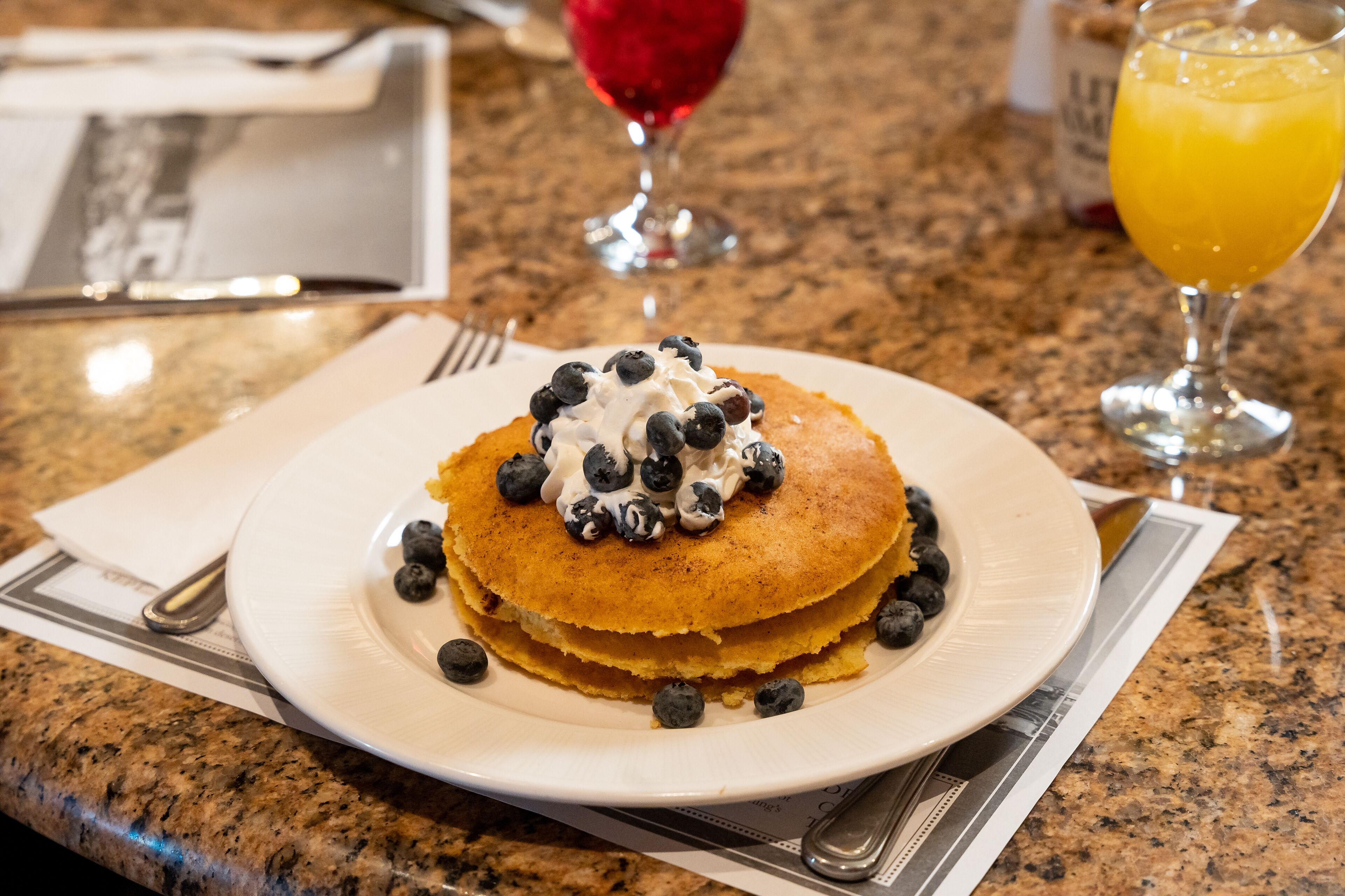 A plate of pancakes with blueberries and whipped cream on a granite countertop.