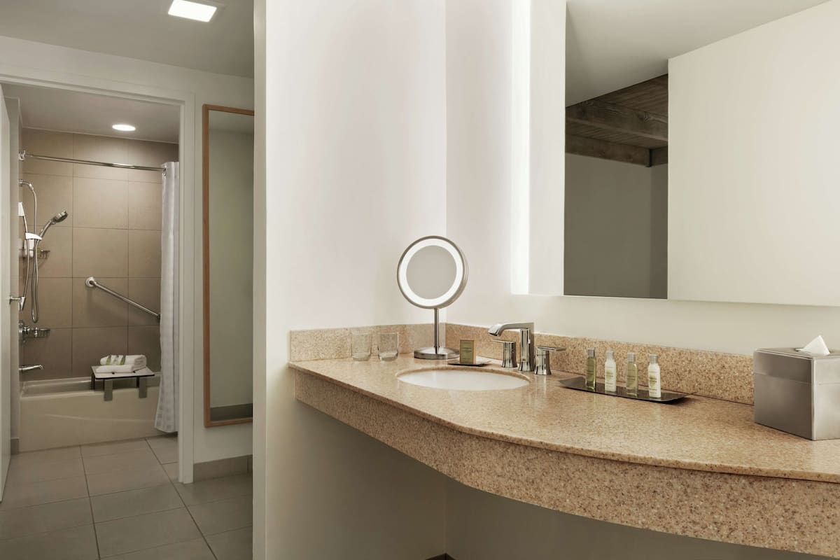 Une salle de bain moderne avec un comptoir en granit, un miroir rond, un lavabo et un espace douche.