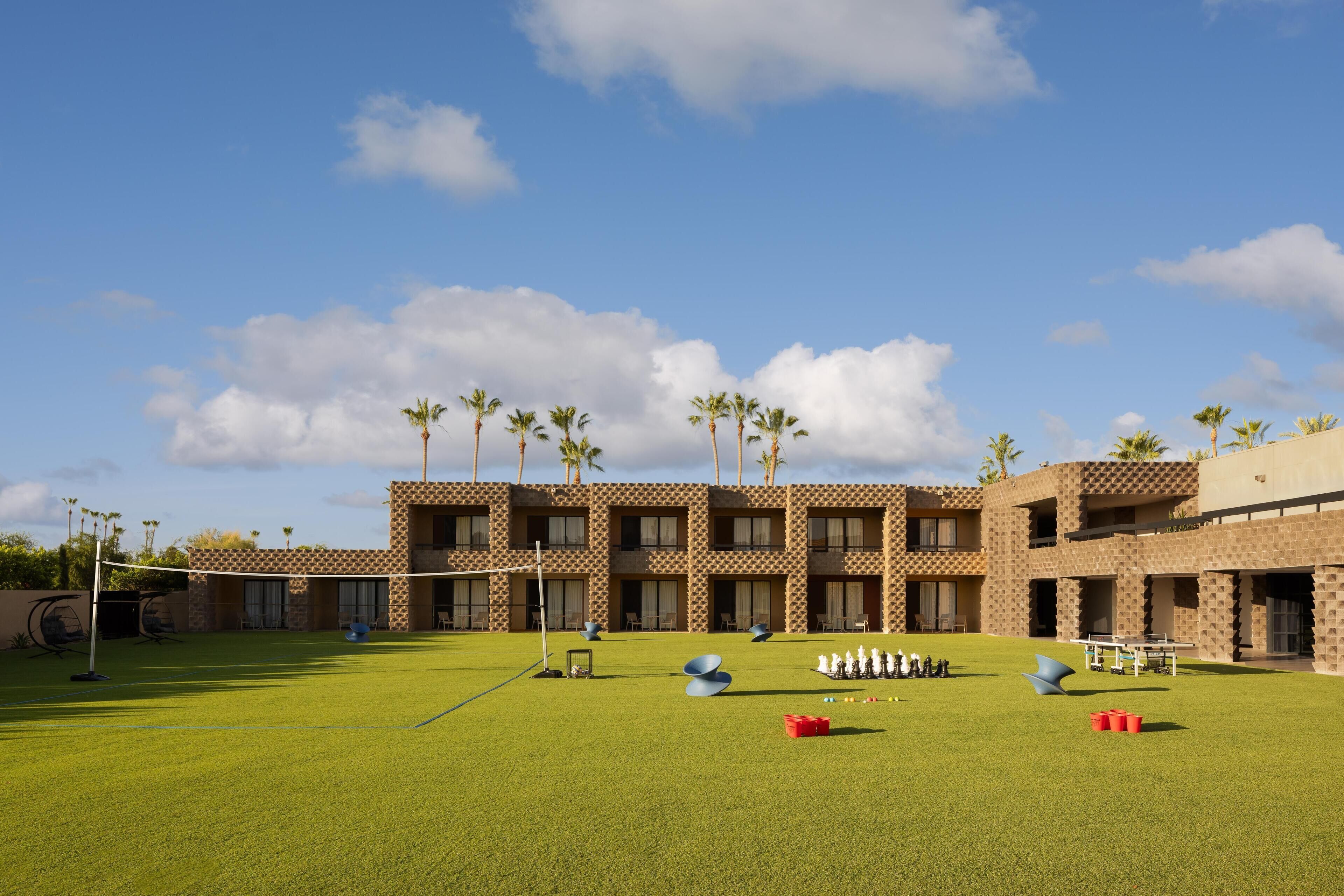 A hotel courtyard with a tennis court, outdoor seating, and palm trees.